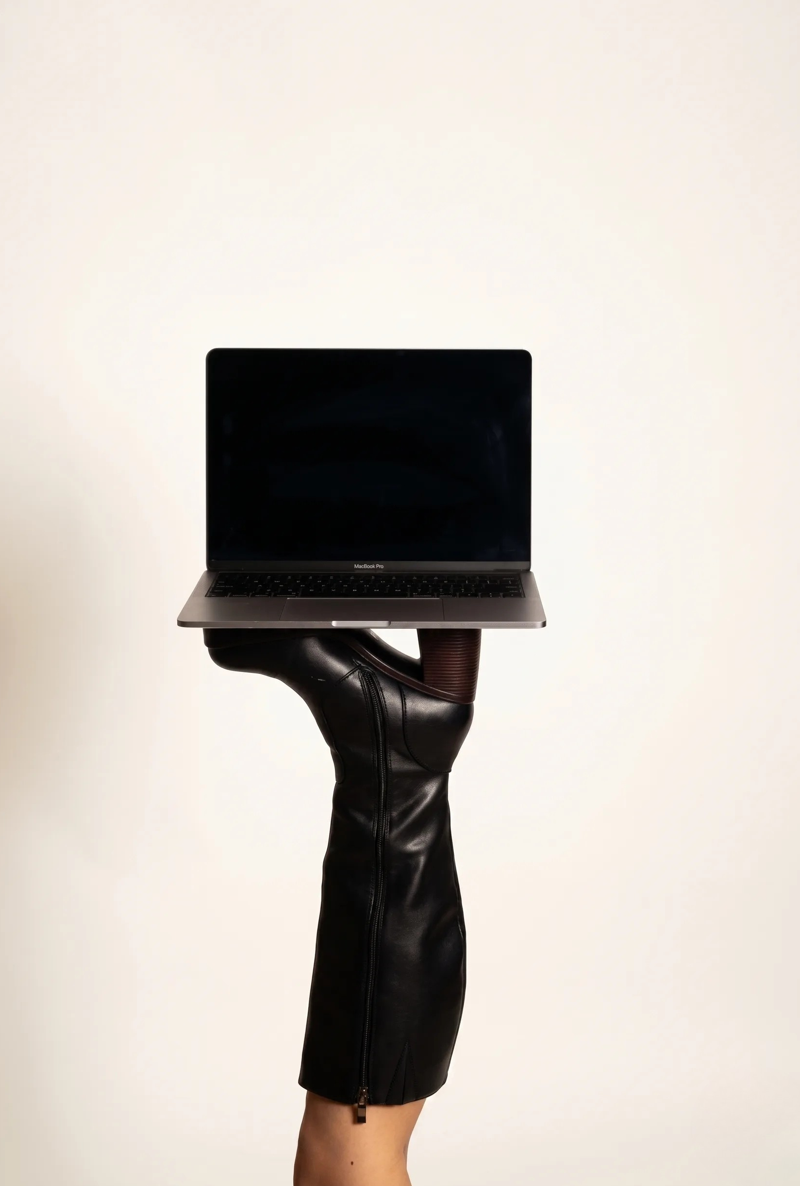 MacBook sostenido por una bota negra de tacón — combinación de tecnología y estilo